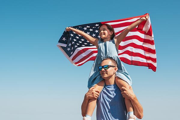 daughter holding american flag riding on dad's shoulders